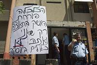 Police officers wait outside while Rachel, a single mother, blockades herself in her home, in an attempt to prevent eviction by the Amidar public housing company, Yavne, April 2008. The placard outside the house reads, &quotThe economy is booming – but the result is that you and I are not included in the deal."<br>Oren Ziv/activestills.org<br>